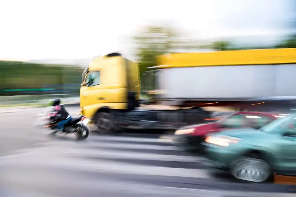 A motorcycle speeding by a truck.