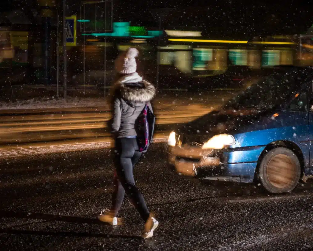 Woman walking across a street in the snow.